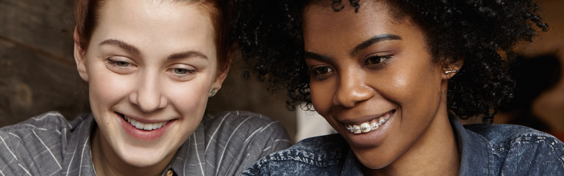 Stylish black lesbian with Afro hairstyle and braces browsing internet or shopping online, using laptop computer together with her attractive white girlfriend. People and modern technology concept